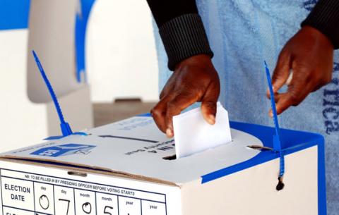 A woman deposits her ballot into a ballot box after voting. Source: GCIS